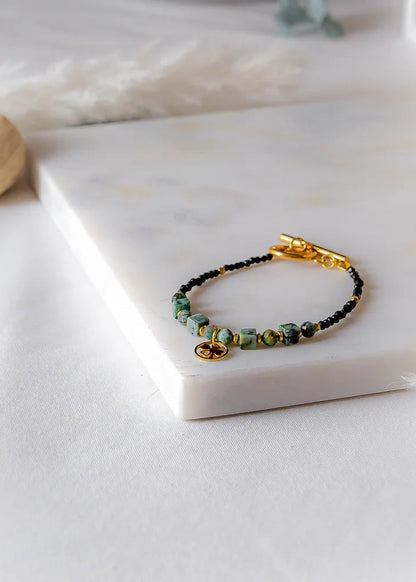 Szczęśliwa Koniczynka Bransoletka Z Turmalinu Czarnego I Turkusu Afrykańskiego Elegancka Biżuteria ułożona na marmurowej desce z czarnymi elementami.