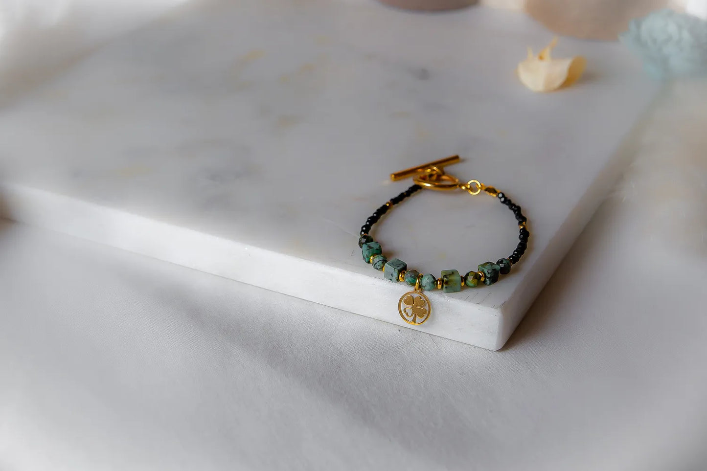 Szczęśliwa Koniczynka Bransoletka: czarne kamienie i zielony turkus afrykański, złota koniczynka, na białym tle.