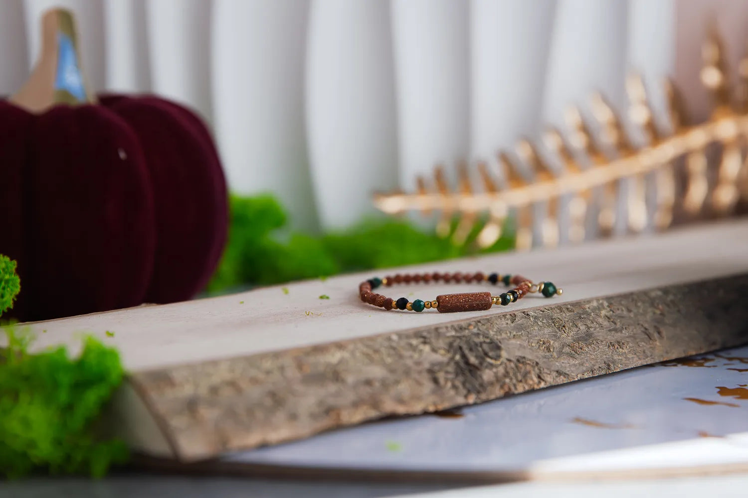 SZEPT LASU - BRANSOLETKA Z PIASKU PUSTYNI, AGATU I TURMALINU. Bransoletka z kolorowymi koralikami, w tym piasku pustyni, agatem i turmalinem, leży na drewnianym tle z zielonymi liśćmi w tle.