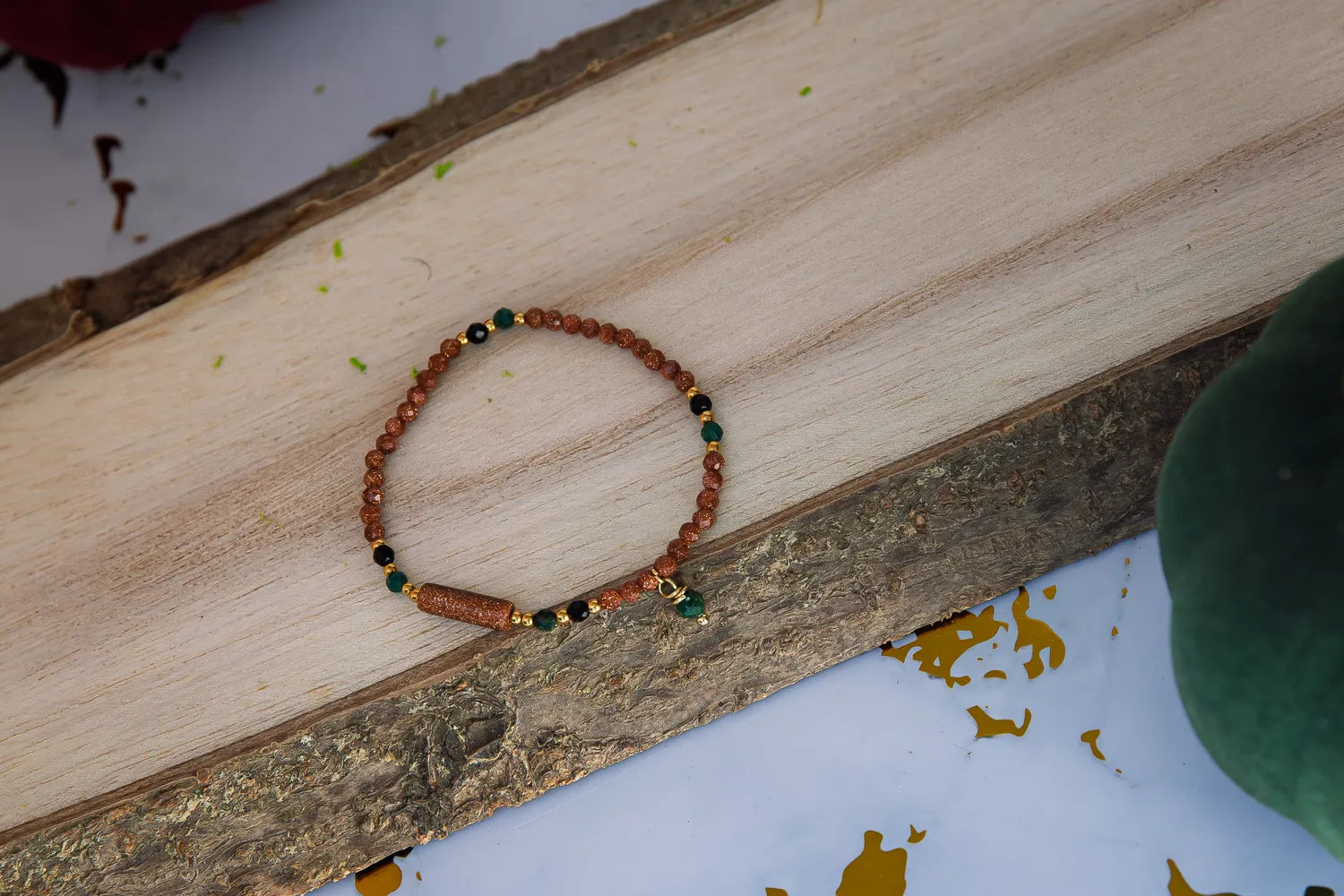 SZEPT LASU - BRANSOLETKA Z PIASKU PUSTYNI, AGATU I TURMALINU. Bransoletka z koralikami piasku pustyni, agatu i turmalinu leży na drewnianym tle, ułożona w kształt koła.