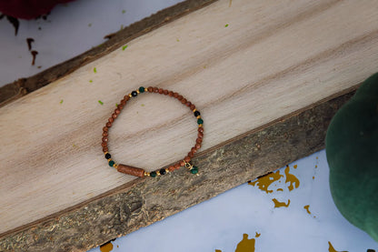 SZEPT LASU - BRANSOLETKA Z PIASKU PUSTYNI, AGATU I TURMALINU. Bransoletka z koralikami piasku pustyni, agatu i turmalinu leży na drewnianym tle, ułożona w kształt koła.