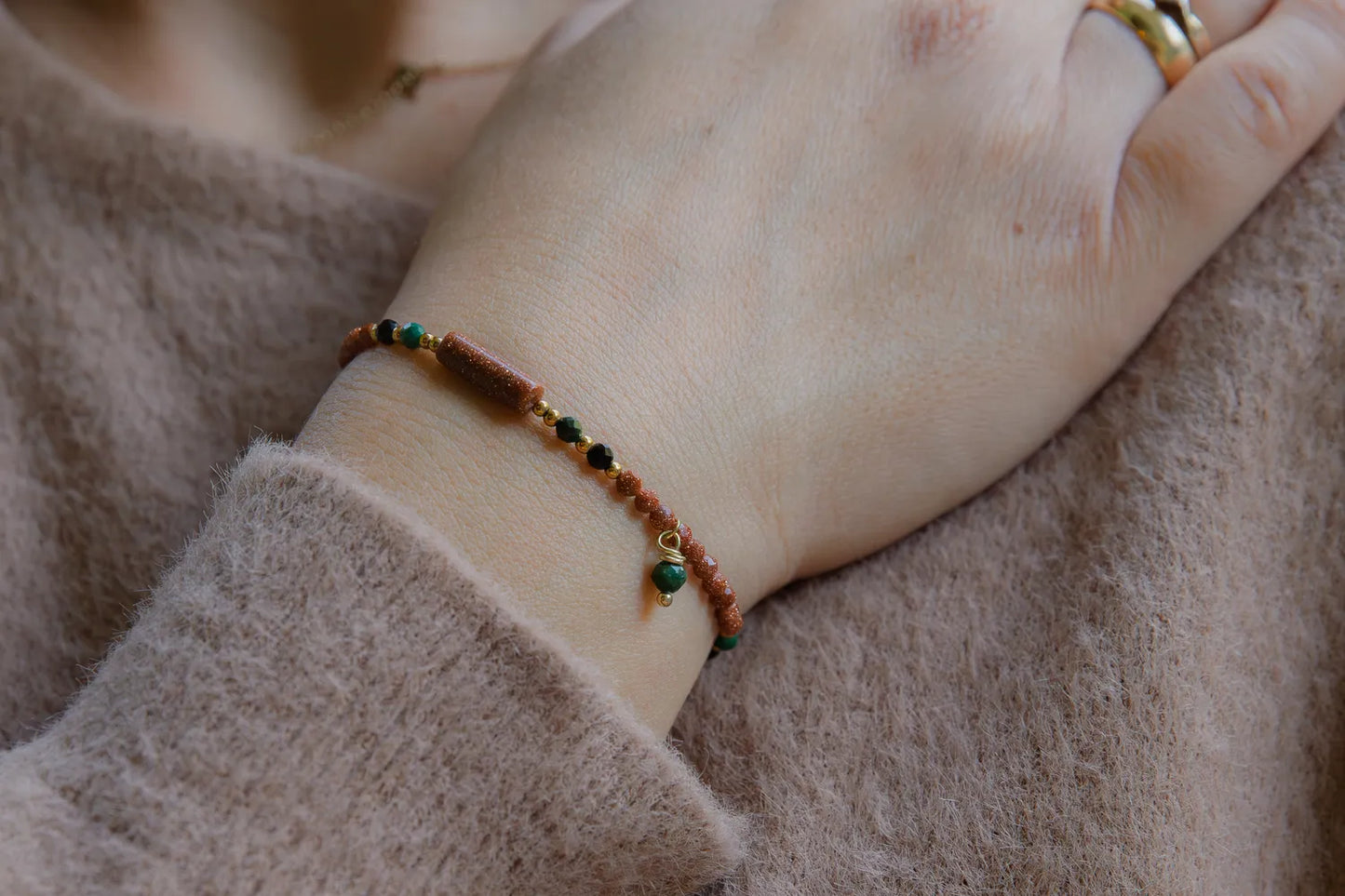 SZEPT LASU - BRANSOLETKA Z PIASKU PUSTYNI, AGATU I TURMALINU. Bransoletka z koralikami z piasku pustyni, agatu i turmalinu na delikatnej dłoni, tło z miękkiej tkaniny.