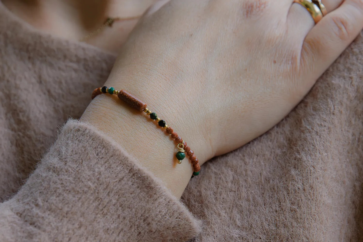 SZEPT LASU - BRANSOLETKA Z PIASKU PUSTYNI, AGATU I TURMALINU. Bransoletka z koralikami z piasku pustyni, agatu i turmalinu na delikatnej dłoni, tło z miękkiej tkaniny.
