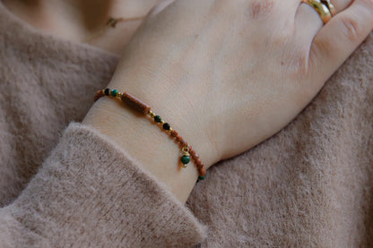 SZEPT LASU - BRANSOLETKA Z PIASKU PUSTYNI, AGATU I TURMALINU. Bransoletka z koralikami z piasku pustyni, agatu i turmalinu na delikatnej dłoni, tło z miękkiej tkaniny.