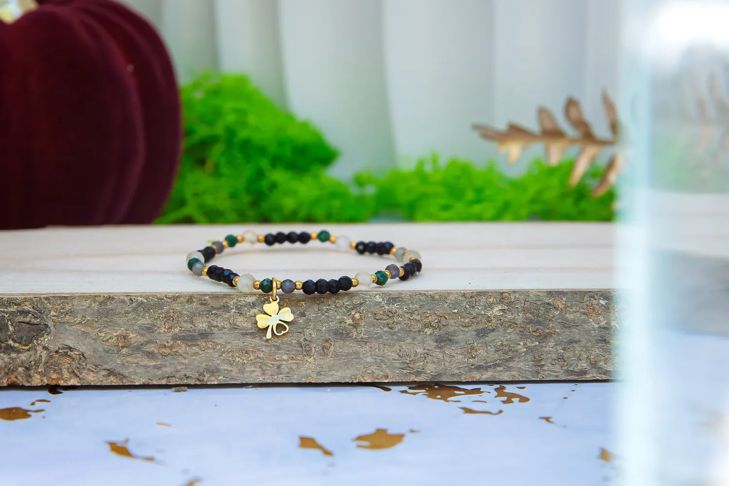 SZEPT SZMARAGDOWEJ WYSPY - BRANSOLETKA Z LEPIDOLITU, CYTRYNU I LABRADORYTU. Bransoletka szczęścia z koniczynką prezentowana na drewnianej belce w otoczeniu zieleni.