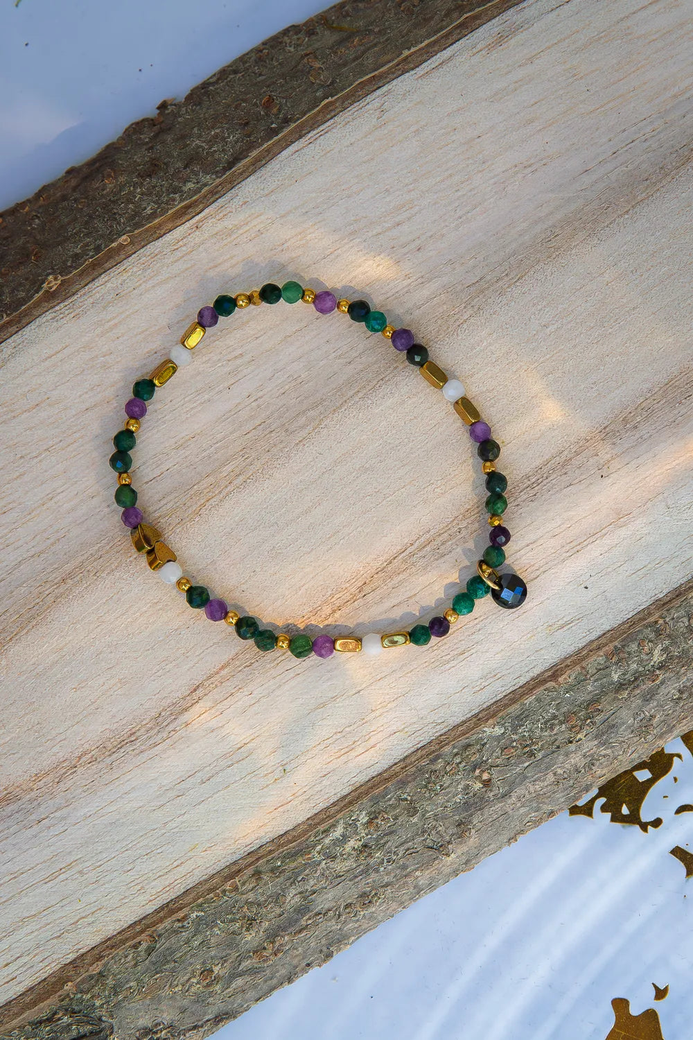 TAJEMNY OGRÓD - BRANSOLETKA Z LEPIDOLITU I CHALCEDONU, elegancka bransoletka z kolorowymi kamieniami lepidolitu i chalcedonu, ułożona na naturalnym drewnianym tle.