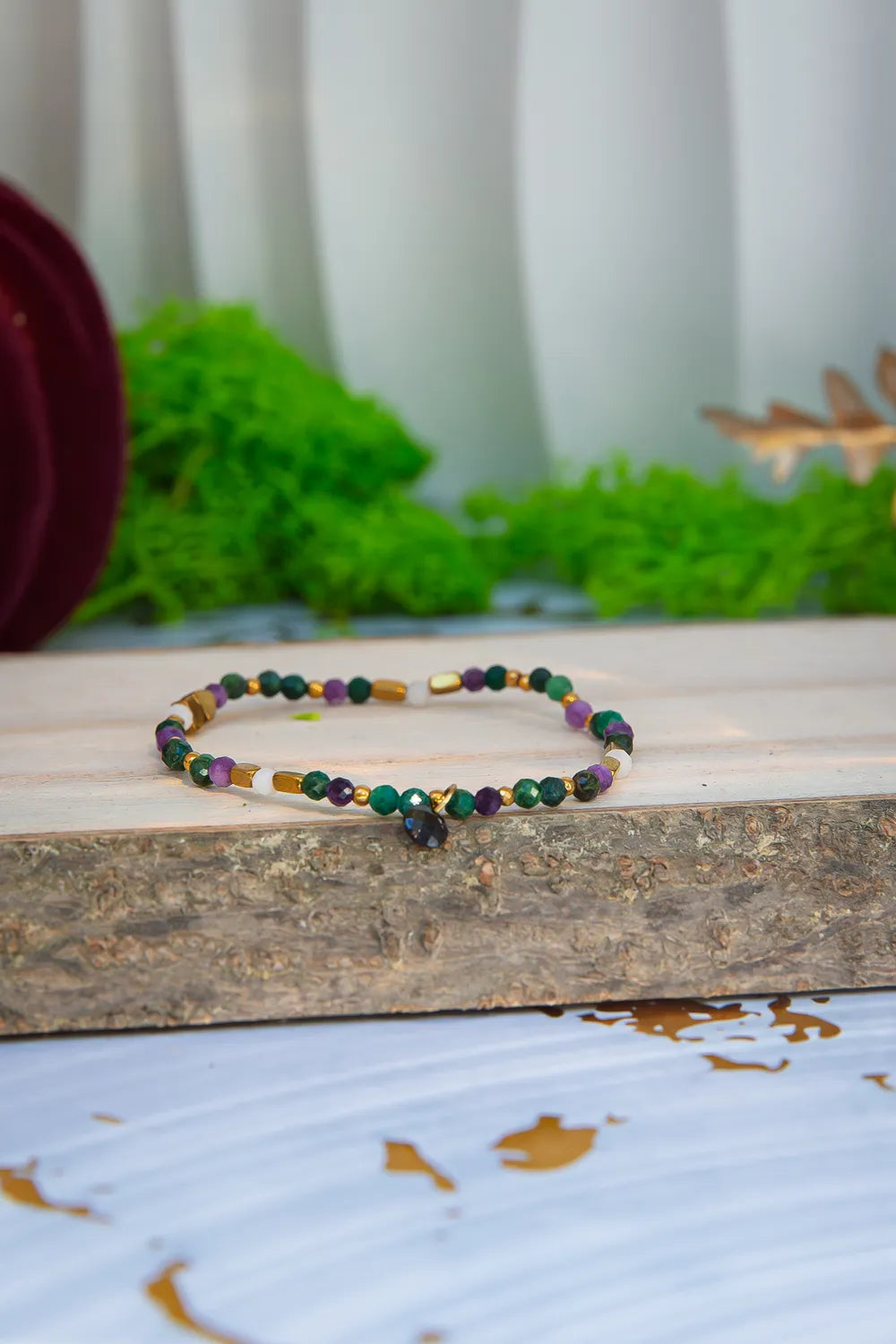 TAJEMNY OGRÓD - BRANSOLETKA Z LEPIDOLITU I CHALCEDONU, bransoletka z kolorowymi kamieniami lepidolitu i chalcedonu, ułożona na drewnianym bloku z zielonym mchem w tle.