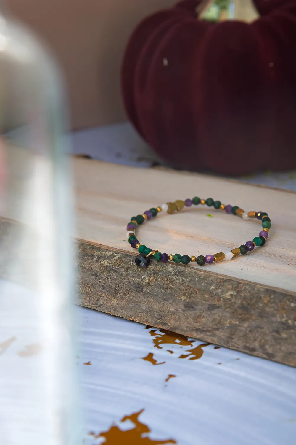 TAJEMNY OGRÓD - BRANSOLETKA Z LEPIDOLITU I CHALCEDONU, elegancka bransoletka z kolorowymi kamieniami lepidolitu i chalcedonu, ułożona na drewnianym tle z czerwoną dynią w tle.