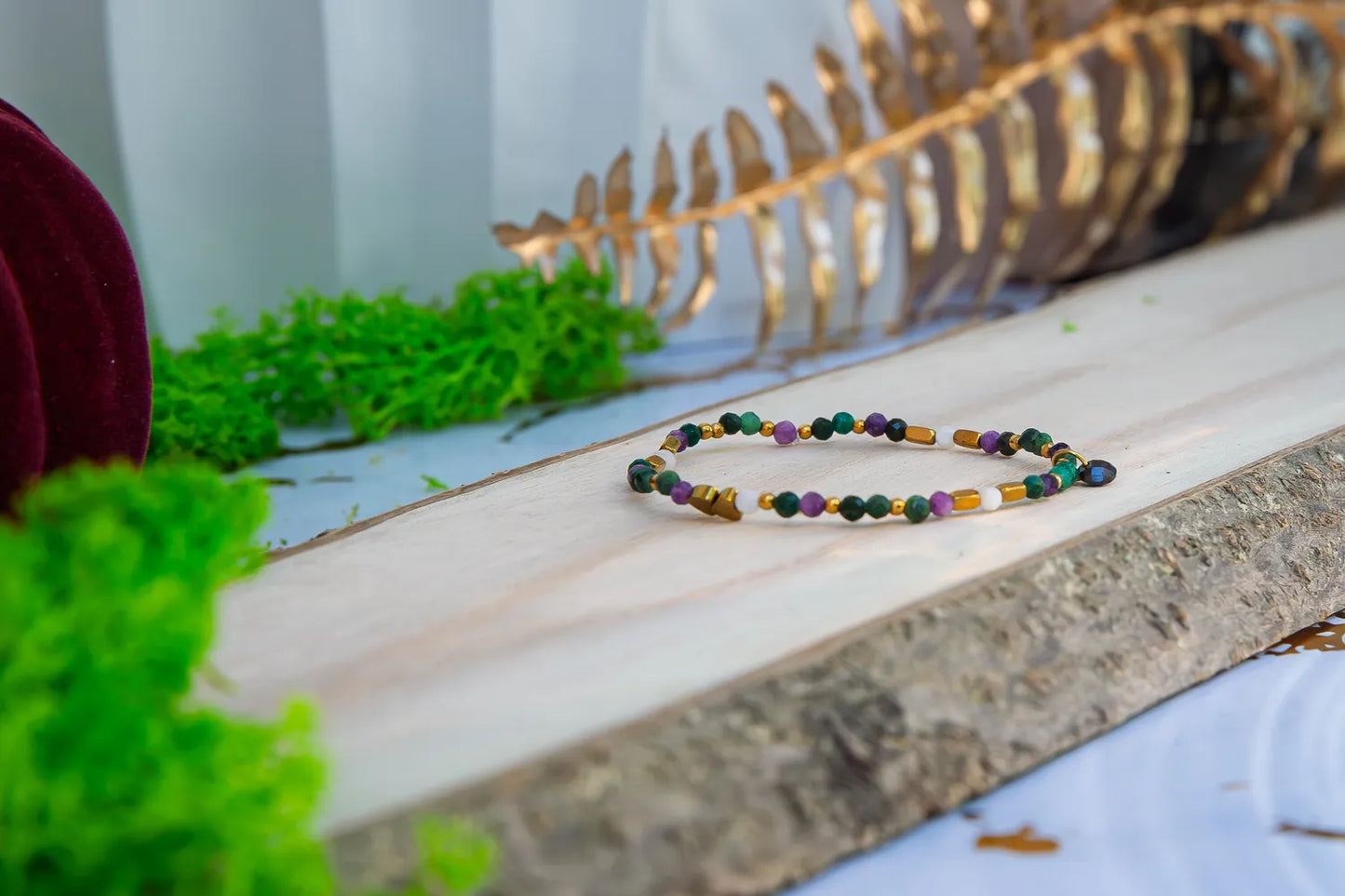 TAJEMNY OGRÓD - BRANSOLETKA Z LEPIDOLITU I CHALCEDONU, złożona z kolorowych koralików lepidolitu i chalcedonu, leżąca na drewnianym pomoście z zielonym mchem w tle.