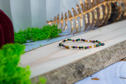 TAJEMNY OGRÓD - BRANSOLETKA Z LEPIDOLITU I CHALCEDONU, złożona z kolorowych koralików lepidolitu i chalcedonu, leżąca na drewnianym pomoście z zielonym mchem w tle.