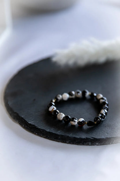 Tao Równowagi Bransoletka Agat Panda Hematyt: okrągłe, wzorzyste kamienie agatu w czerni i bieli, ciemne kamienie hematytu lśnią na czarnej płycie, jasne tło.
