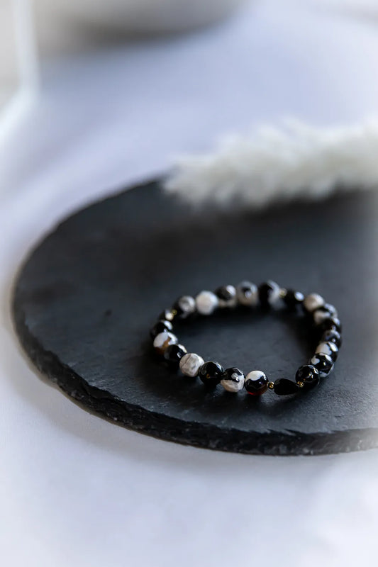 Tao Równowagi Bransoletka Agat Panda Hematyt: okrągłe, wzorzyste kamienie agatu w czerni i bieli, ciemne kamienie hematytu lśnią na czarnej płycie, jasne tło.