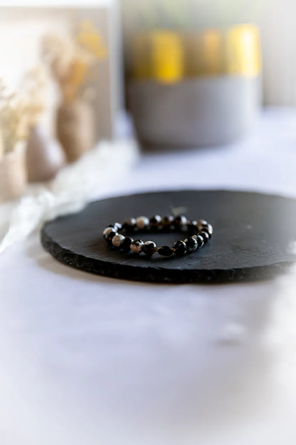 Tao Równowagi Bransoletka Agat Panda Hematyt z błyszczącymi czarnymi i mlecznymi kamieniami, na czarnej wulkanicznej płycie, z subtelnym tłem.