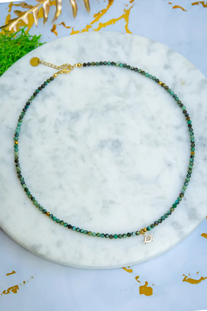 TARCZA ŻÓŁWIA - NASZYJNIK Z TURKUSU AFRYKAŃSKIEGO, naszyjnik z koralikami turkusowymi, zawieszka w kształcie żółwia, tło marmurowe, dekoracja z liści.