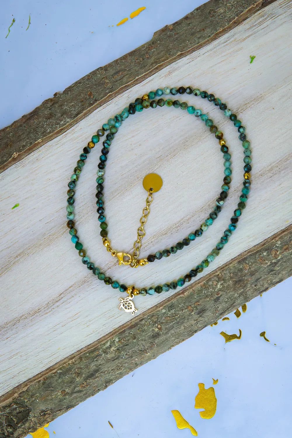 TARCZA ŻÓŁWIA - NASZYJNIK Z TURKUSU AFRYKAŃSKIEGO, naszyjnik z drobnymi koralikami turkusowymi, zawieszka w kształcie żółwia, tło drewniane, ułożenie spiralne.
