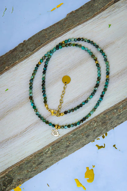 TARCZA ŻÓŁWIA - NASZYJNIK Z TURKUSU AFRYKAŃSKIEGO, naszyjnik z drobnymi koralikami turkusowymi, zawieszka w kształcie żółwia, tło drewniane, ułożenie spiralne.