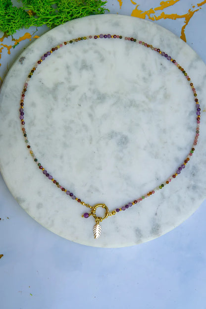 TĘCZOWA AURA - NASZYJNIK Z KOLOROWEGO TURMALINU I GRANATU. Naszyjnik z kolorowymi kamieniami turmalinu i granatu, ułożony na marmurowym tle z dodatkiem złotego liścia.