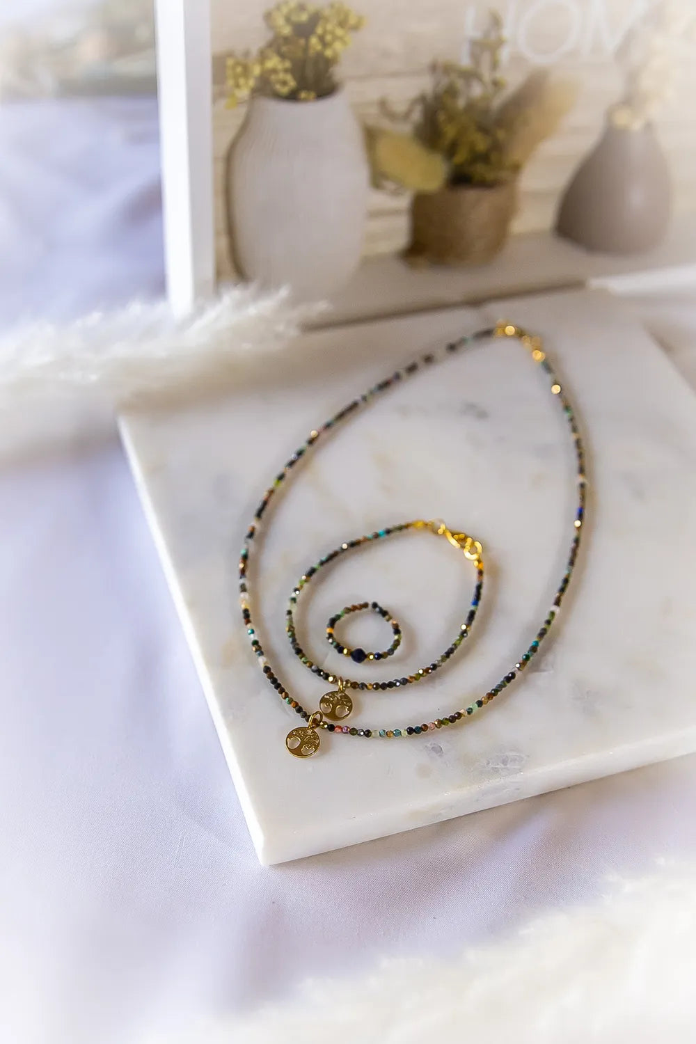 Tęczowa Harmonia Komplet Turmalin Drzewko Szczęścia: złoty naszyjnik i pierścionek z wielobarwnymi turmalinami i zawieszkami drzewka życia na marmurowym tle.