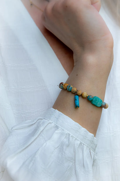 Turkusowa Oaza Bransoletka Z Jaspisu I Turkusu Biust: ręcznie robiona biżuteria z niebieskimi kamieniami i jaspisem, na ręce w białej koszuli.