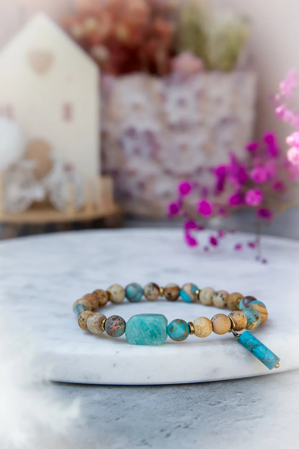 Turkusowa Oaza Bransoletka Z Jaspisu I Turkusu Kwiaty, z centralnym prostokątnym turkusowym kamieniem i wiszącym turkusowym elementem, na tle dekoracji z kwiatów.