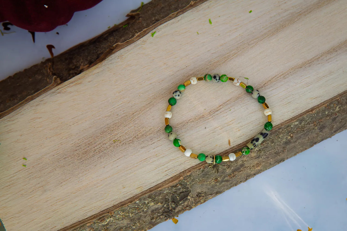 Bransoletka 'TWOJA OAZA' z zielonego jaspisu cesarskiego i howlitu, ułożona na drewnianym tle. Biżuteria ręcznie robiona z kolorowymi kamieniami.