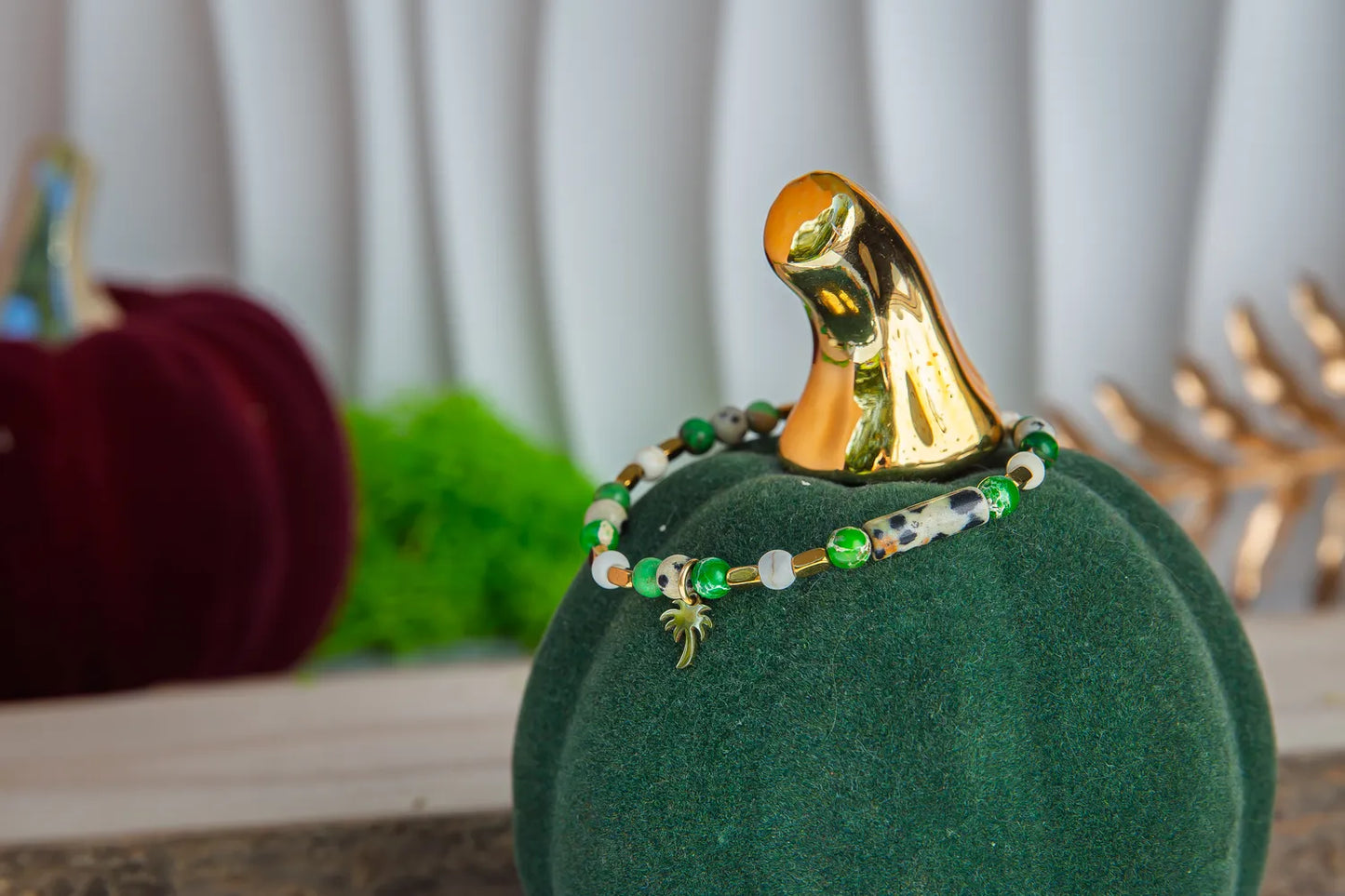 TWOJA OAZA - BRANSOLETKA Z ZIELONEGO JASPISU CESARSKIEGO I HOWLITU, złożona z zielonych kamieni i białych perł, prezentowana na zielonym podstawce w kształcie dyni, z dodatkowym złotym elementem w tle.