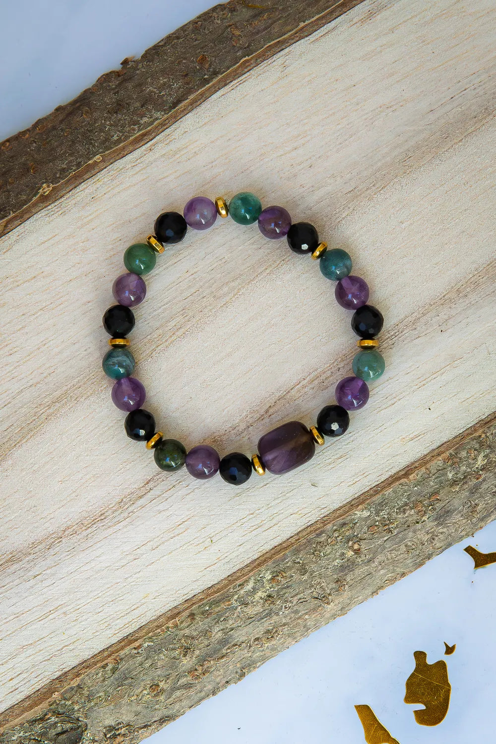 WRZOSOWA NOC - BRANSOLETKA Z AMETYSTU I AGATU INDYJSKIEGO, złożona z kolorowych koralików ametystu, agatu indyjskiego i czarnych kamieni, ułożona na naturalnym drewnianym tle.