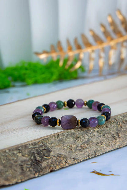 WRZOSOWA NOC - BRANSOLETKA Z AMETYSTU I AGATU INDYJSKIEGO, prezentująca się na drewnianym tle z kamieniami ametystu i agatu indyjskiego, z zielonym mchem i złotym elementem w tle.