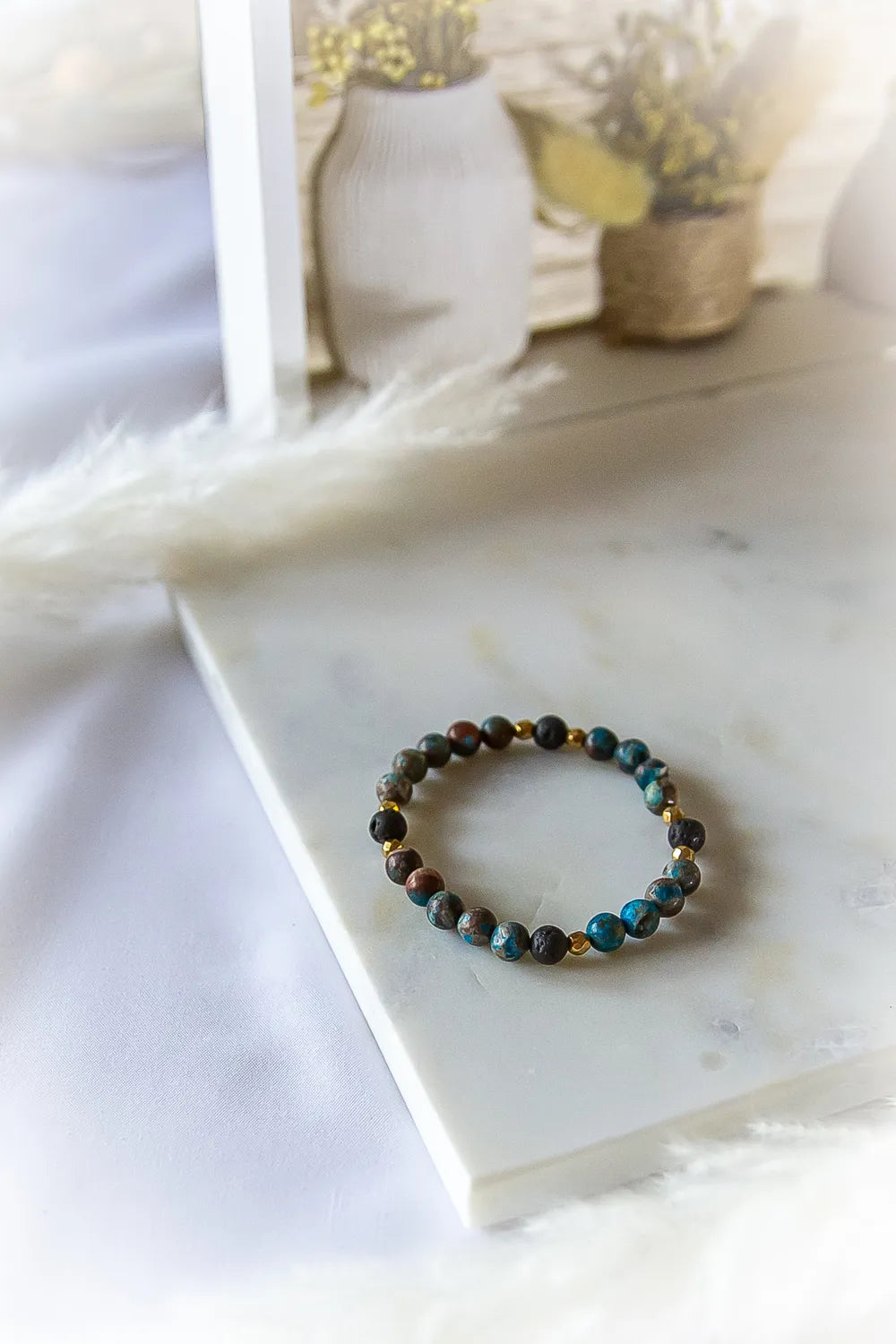 Wulkaniczna Moc Bransoletka Z Turkusem I Lawą: z bliska, kamienie turkusowe i wulkaniczne, złote przekładki, na białej marmurowej podstawie.