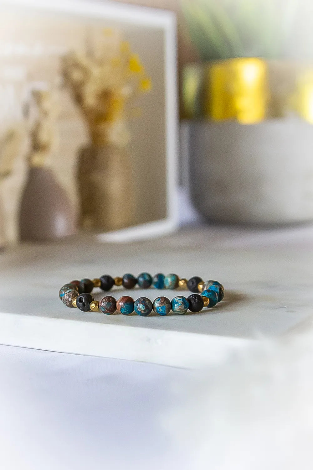 Wulkaniczna Moc Bransoletka Z Turkusu I Lawy Kamienie - zbliżenie na koraliki z turkusu i lawy na tle jasnego blatu i subtelnie rozmytych elementów dekoracyjnych.