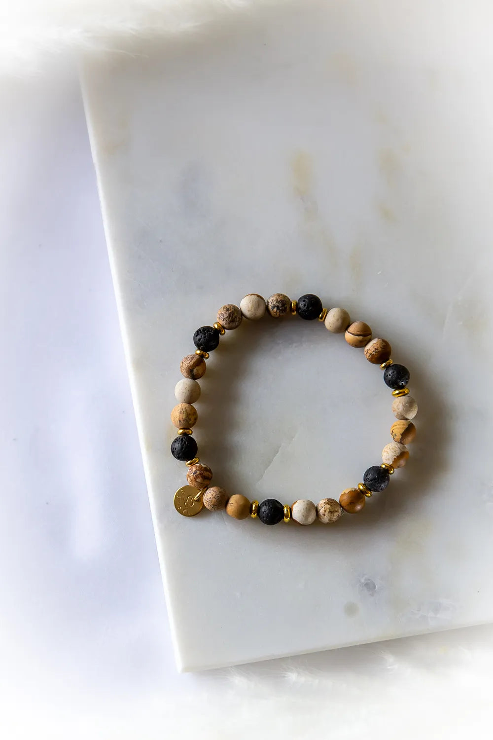 Ziemski Rytm Bransoletka Jaspis Lawa z wyrazistymi kamieniami jaspisu, czarną lawą i złotymi przekładkami na marmurowym tle.