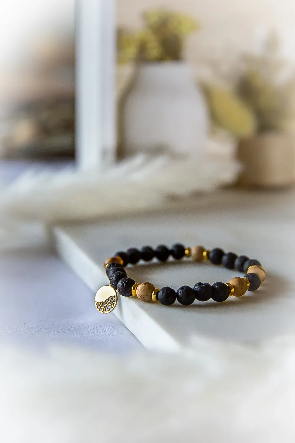 Ziemskie Ścieżki Bransoletka Jaspis Czarna Lawa – kompozycja matowych czarnych kamieni lawy wulkanicznej, jasnego drewienka i złotych przekładek. Bransoletka z zawieszką o zwierzęcym wzorze.