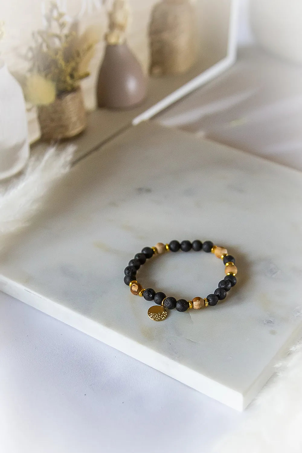 Ziemskie Ścieżki Bransoletka Jaspis Czarna Lawa na marmurowej powierzchni, w tle suche kwiaty.