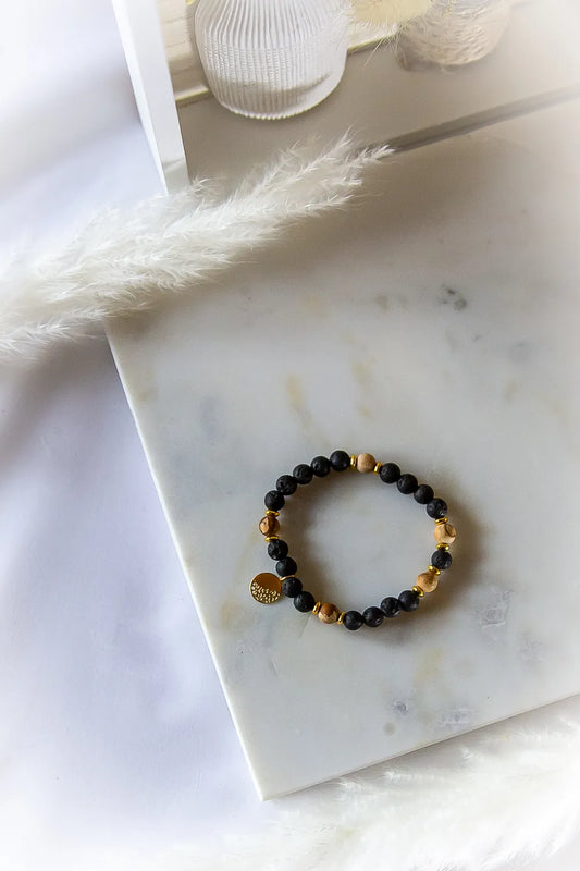 Ziemskie Ścieżki Bransoletka Jaspis Czarna Lawa z kamieni lawy i jaspisu na białym marmurze, ozdobiona złotym medalionem.