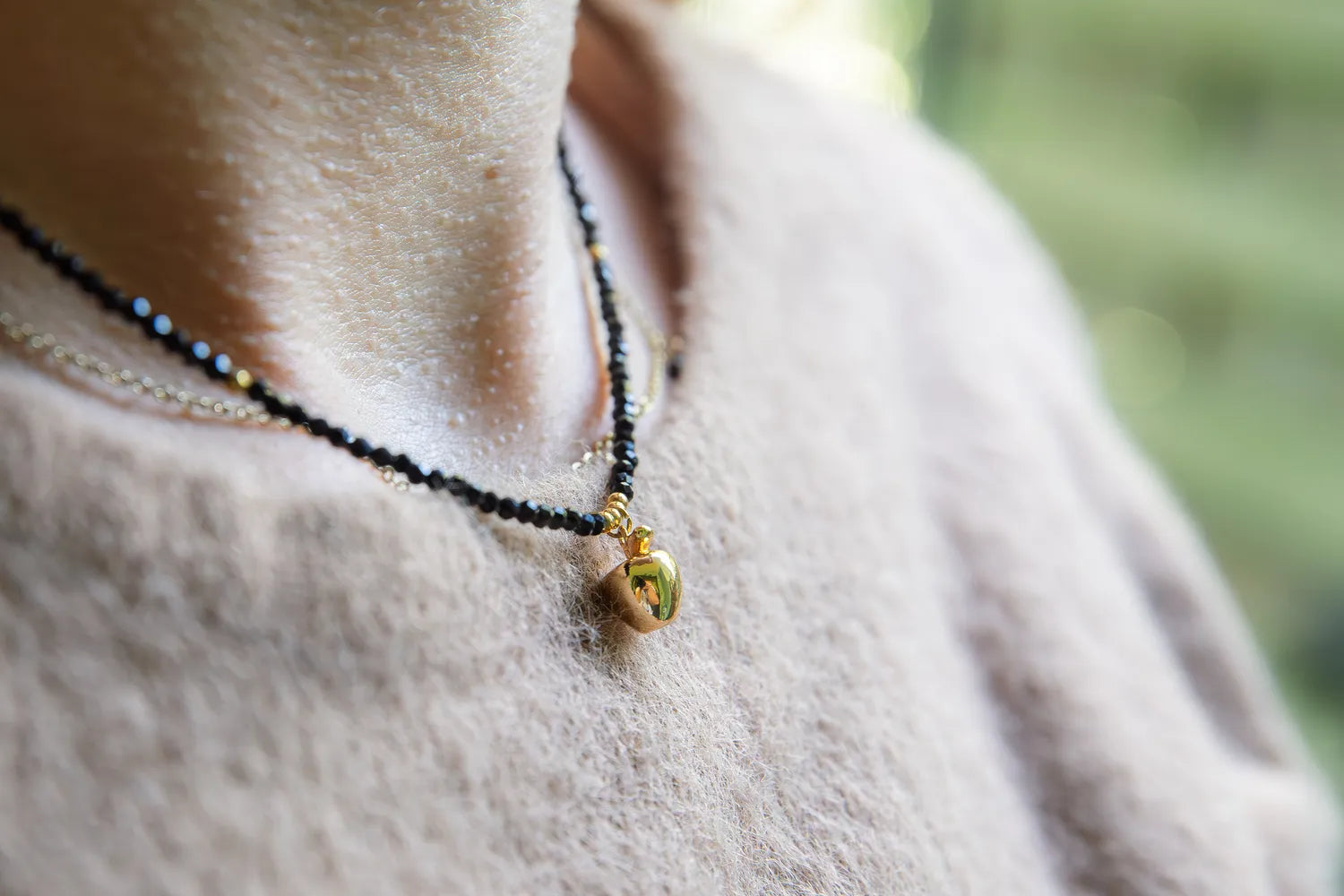 ZŁOTE JABŁKO - NASZYJNIK Z CZARNEGO TURMALINU. Naszyjnik z czarnymi koralikami turmalinu i złotym jabłkiem na delikatnym tle bluzki.