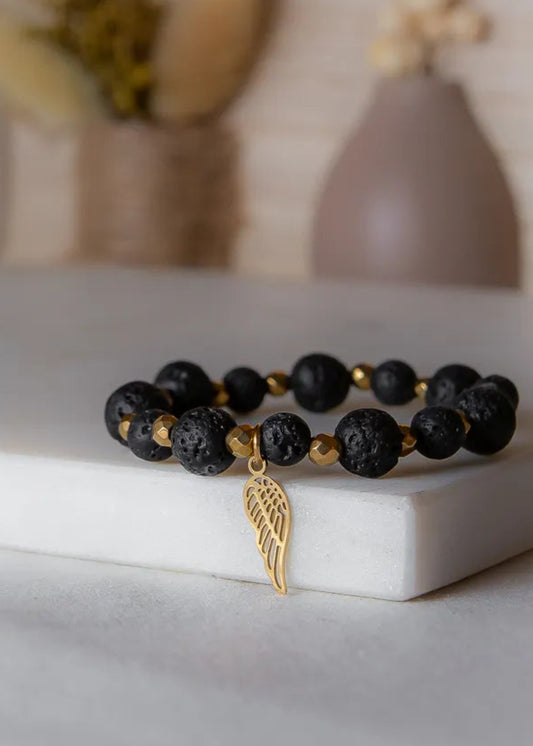 Złote Skrzydło Bransoletka Czarne Kamienie z matowymi, czarnymi kamieniami i złotymi hematytami, ozdobiona zawieszką skrzydła.